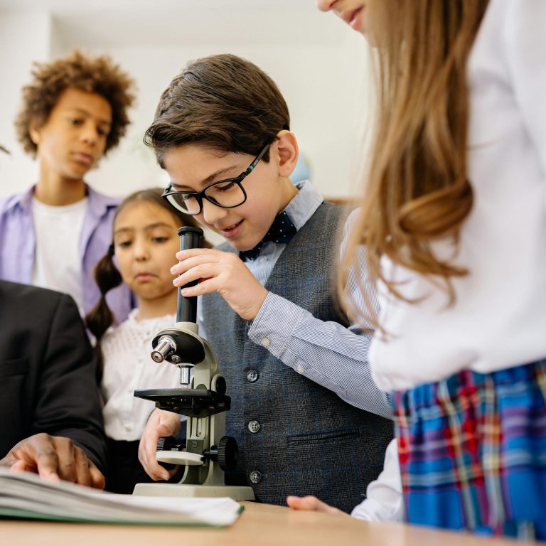 Children in a classroom exploring science with a microscope, emphasizing learning and diversity.