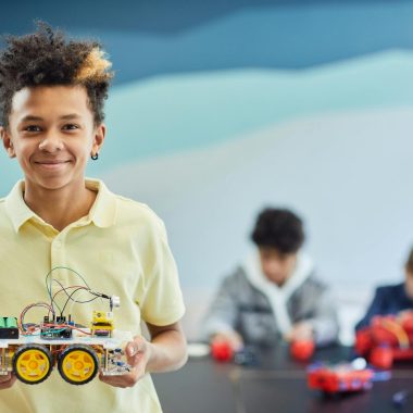 Smiling student holds robotics project during a hands-on STEM activity in the classroom.