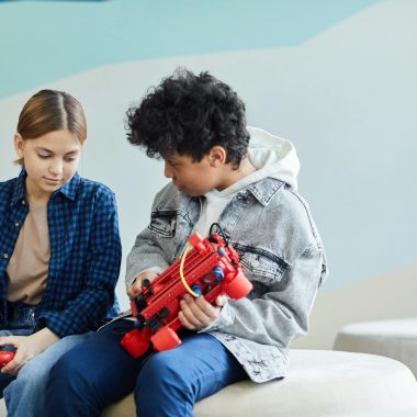 Two teenagers sitting and collaborating on a robotics project in a casual indoor setting.