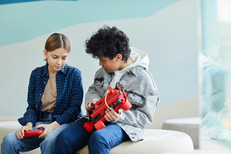 Two teenagers sitting and collaborating on a robotics project in a casual indoor setting.